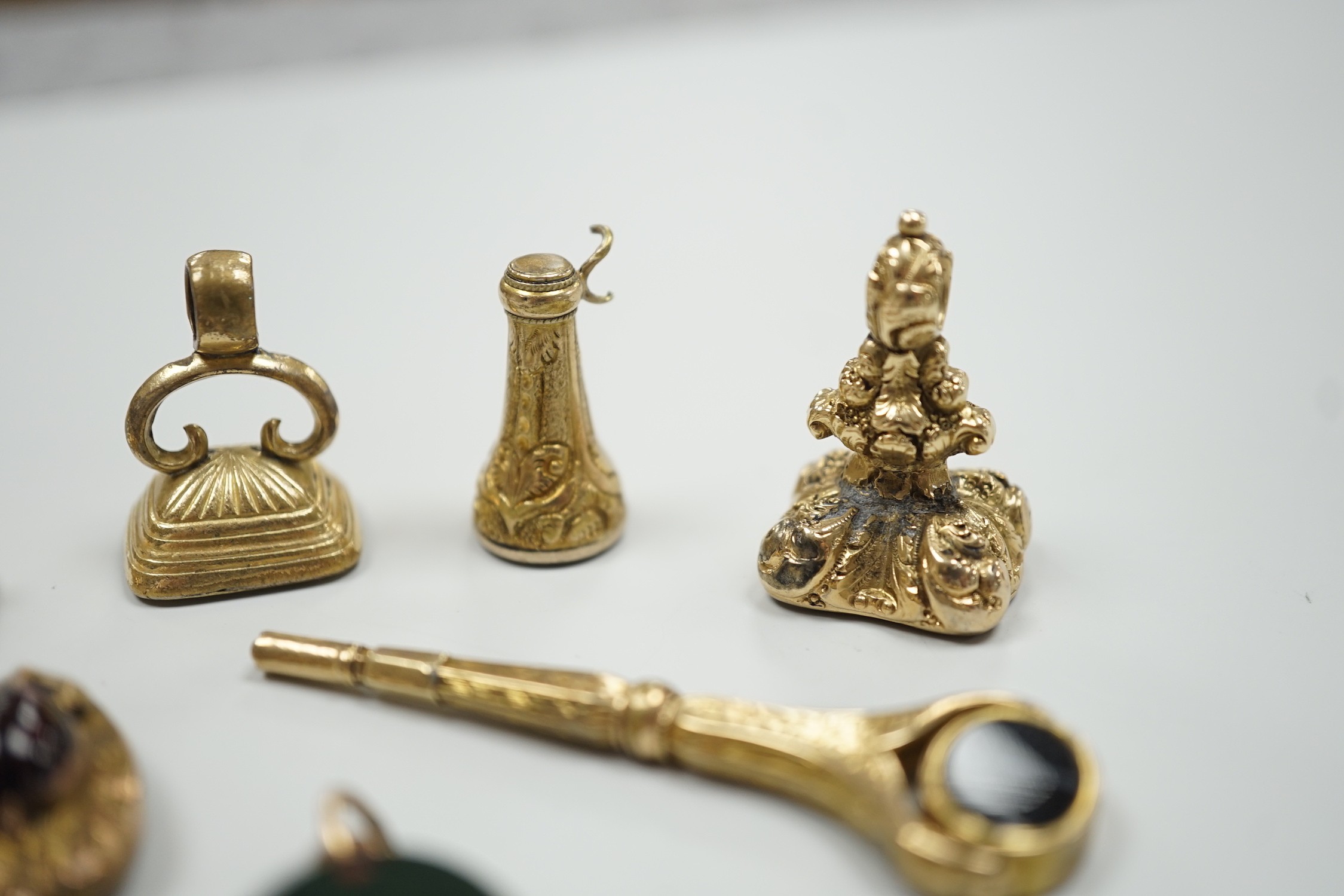 Four assorted 19th century and later yellow metal overlaid and gem set fob seals, a Victorian 15ct gold and sardonyx spinning fob, a sardonyx set locket, damaged pendant and yellow metal and two stone set watch key.